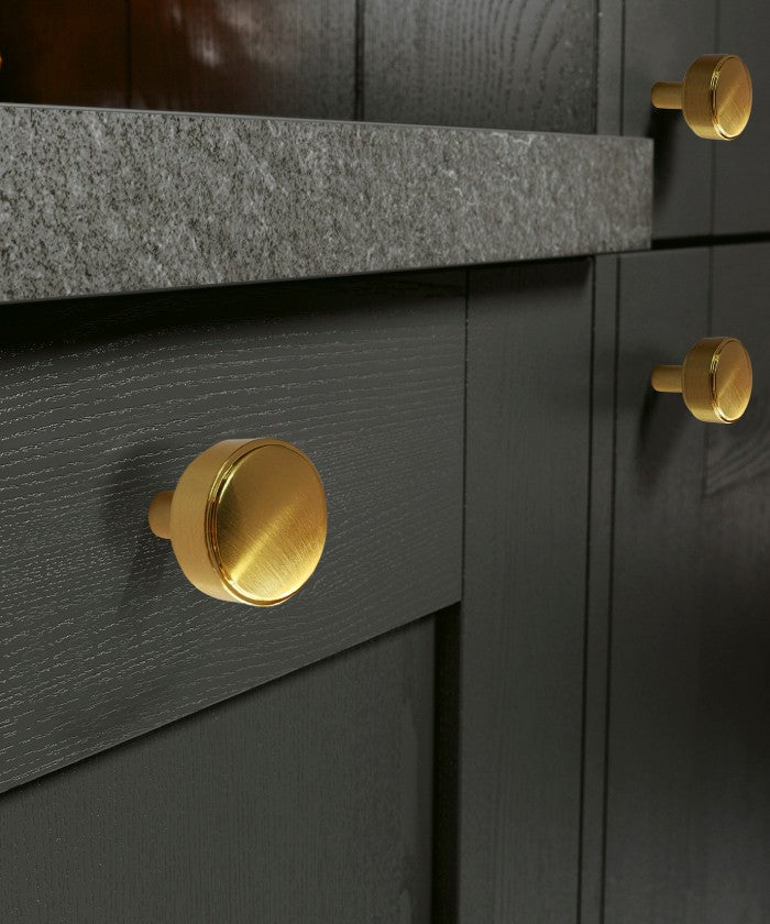 Brushed Gold Wilmont Round Knobs Mounted on Black Kitchen Cabinet